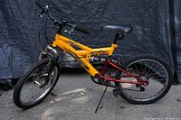 Side view of Supercycle 600DS kids bicycle showing yellow and black frame with red rear suspension and flat tires.
