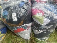 Two large clear plastic bags filled with mixed men's and women's clothing stacked outdoors on grass.