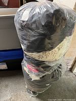 Two very large plastic bags tightly packed with assorted clothing, sealed in clear plastic wrapping.
