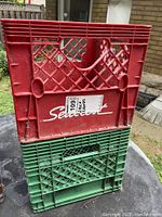 Two plastic milk crates stacked, one red with 'Schmidt' label and one green below it, showing age wear and typical usage marks.