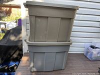 Two stacked Rubbermaid storage bins, one beige on top and one gray on bottom, placed outside.