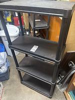 Black plastic 4-shelf shelving unit showing full height and shelf design