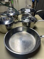 Five-piece Paderno stainless steel pots and pan set displayed on a table, showing pots with lids and a frying pan.