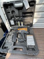 Gas Bostitch nailer in black molded plastic carrying case with two gas cartridges inside.