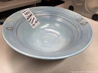 Photo of wide light blue pottery bowl showing interior with light brush marks and bicycle illustrations.