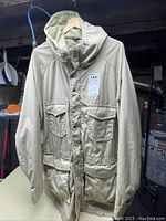 Front view of beige Eddie Bauer men's jacket with multiple flap pockets and hood hung on a hanger