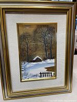 Photo of the framed print showing the winter snowy landscape with a cabin and trees in a gilded wood frame.