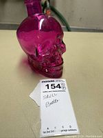 Side view of a purple glass skull-shaped bottle placed on a flat surface with a label reading 'SKULL Bottle'.