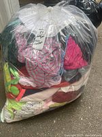 Large sealed plastic bag filled with assorted kids clothes featuring visible pink and striped tops among other clothing.