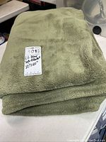 Photo of folded, olive-green L.L. Bean sofa blanket with a label indicating size 80x60 inches.
