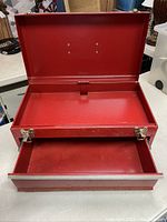 Opened view of the red metal tool box showing the hinged lid and empty inner compartment along with the pull-out drawer open at the front.