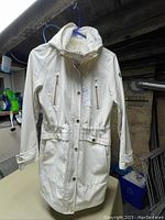 Front view of white Michael Kors jacket hanging, showing the full length, button and zipper closure, front pockets, adjustable waist detail, and hood.