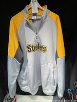 Front view of the light grey and gold Steelers jersey with embroidered logo and quarter zip.