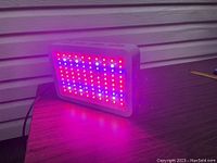 Rectangular LED grow light panel turned on, emitting red, blue, and white light, placed on wooden table.
