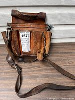 Front and side view of vintage leather tool pouch showing multiple pockets, stitching, rivets, and attached adjustable leather shoulder strap.