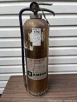 Full view of vintage brass fire extinguisher with attached hose and pressure gauge, displaying wear and original label.