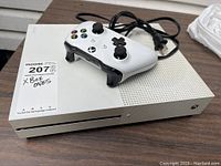 Front view of white Xbox One S console with wireless controller and power cable on tabletop