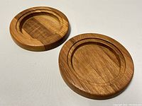 Two round teak wine bottle coasters showing natural wood grain and circular grooved design for bottles. Minor surface wear visible.