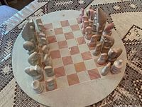 Full overhead view of round soapstone chessboard with all 32 pieces arranged in starting positions, set on patterned tablecloth.