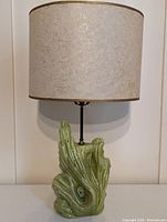Front view of vintage pottery table lamp with green ceramic base shaped like driftwood and cream textured shade.