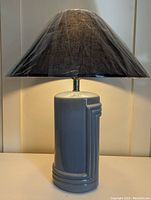 Side view of Deco Revival ceramic lamp with linen shade wrapped in plastic, showing geometric detailing on the grey cylindrical base