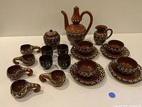 Overview of entire vintage tea and drink set showing cups, saucers, sugar pot, creamer jug, and decanter/tea pot with consistent hand-painted Troyan design.