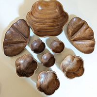 Top-down view of all nine wooden serving bowls arranged on a white surface, showing flower and petal shapes and different sizes.