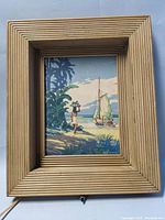 Front view of framed electric lamp with South Pacific scene artwork showing a woman carrying a basket, tropical foliage and sailboat by the shore.