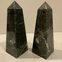 Pair of polished black granite obelisks from front angle on beige background