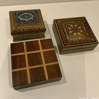 Front and top view of three vintage decorative wooden boxes showing various wood patterns and designs.