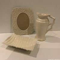Three vintage cream decorative items including a pitcher, photo frame, and rectangular dish shown together.
