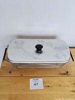 Top view of aluminum lid with engraved floral design and black knob on wooden surface.