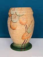 Full view of vintage Duchess pottery vase against blue background, showing hand-painted Art Nouveau leaves in green and orange on beige body with green base.