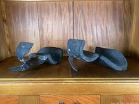 Pair of vintage anti-gravity boots displayed side by side showing curved soles and molded foot moldings on wood surface with wood backdrop.