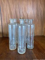 Photo showing all six clear glass apothecary bottles standing upright on a wooden surface with wood paneling background.