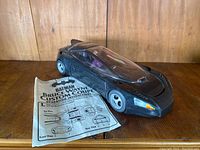 Photo shows black 1991 Batman Returns Bruce Wayne Custom Coupe toy vehicle with clear canopy and detailed body, together with folded instruction sheet bearing title and diagrams.
