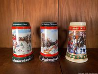 Front view of all three Budweiser Christmas steins, showing detailed winter scenes and decorative bases.