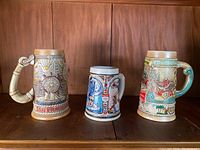 Front view of three Budweiser steins on wooden surface showing detailed artistic designs