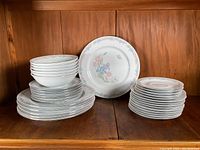 Full display of the 32-piece partial set including stacks of bowls, dinner plates, patterned and plain salad/bread plates, and saucers on a wooden shelf.