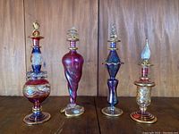 View showing all four mouth-blown perfume bottles with varied shapes and colored glass against wood background