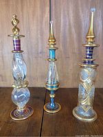 Three Egyptian mouth-blown perfume bottles displayed side by side on wooden surface showing overall designs and colors.