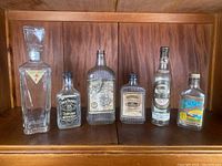 Photo showing six vintage liquor bottles arranged on wood shelf: various brands and sizes, original labels present, light wear visible