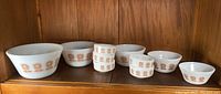 Photo showing five graduated white milk glass mixing bowls and five small prep bowls with orange floral motif, arranged on wooden shelf.