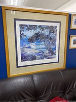 Full view of the large framed print showing the harbor scene framed in a light oak wooden frame with double matting, sitting on a dark couch.