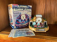 Photo showing Lionel 100th Anniversary alarm clock with original box and certificate on wooden surface.