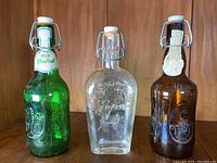 Three vintage glass bottles with swing-top caps placed side by side on a wooden shelf.