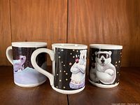 Front and side views of three Coca Cola polar bear mugs showing different bear designs on black starry backgrounds