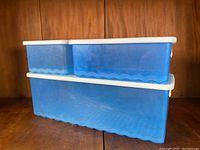 Front view of two stacked blue Tupperware fridge keepers with white lids on a wooden shelf.