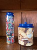 Tall cylindrical vacuum canister filled with colorful wrapped candies and blue vacuum lid on top, sitting on wood shelf