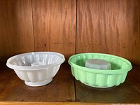 Two vintage Tupperware dessert molds, white and green, side by side on wooden surface.